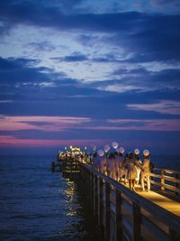 Rear view of crowd walking on jetty against cloudy sky