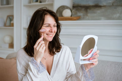 Woman massages her face with pink stone roller, facial massage at home, spa