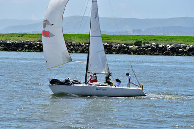 People sailing on sailboat in sea against sky