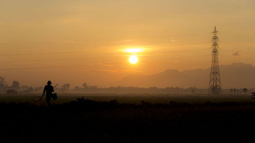 Silhouette man working on landscape against sky during sunset