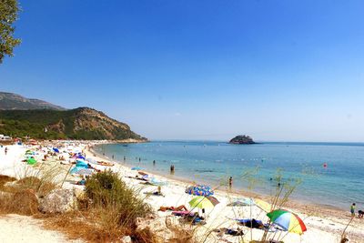 People on beach against clear blue sky