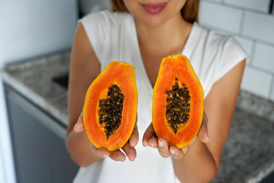 Unidentified young woman showing a papaya cut into two halves in the kitchen