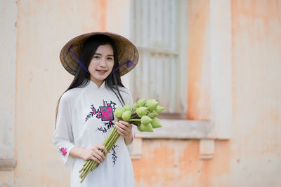 Portrait of smiling young woman holding buds against old building