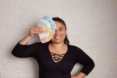 Portrait of smiling young woman holding camera against wall