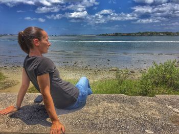 Young woman sitting on retaining wall against sea