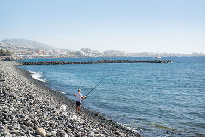 Man fishing in sea against sky