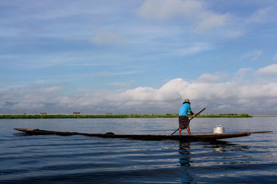 Rear view of man standing on boat in lake against sky