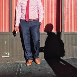 Low section of man smoking while standing by shadow against wall