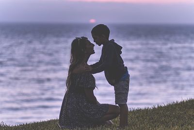 Side view of mother and son on grassy shore during sunset