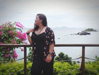 Woman standing by railing against sea 