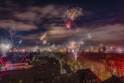 Firework display in city against sky at night