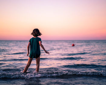 Rear view of woman standing on beach during sunset