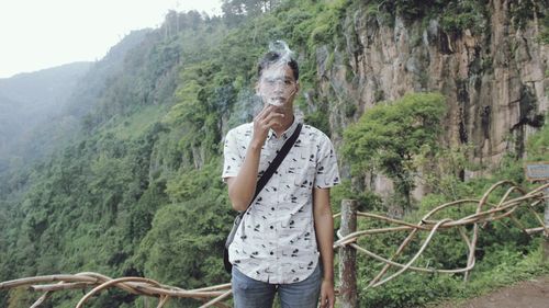 Portrait of young man smoking cigarette against mountains