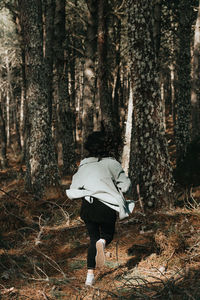 Rear view of woman walking amidst trees in forest