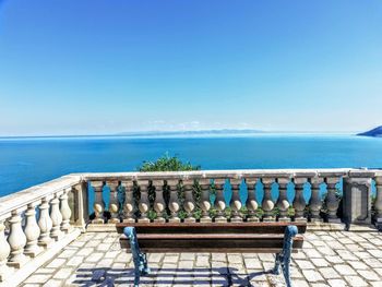 People by swimming pool against sea against clear blue sky