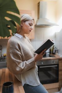 Woman stands reading book in kitchen