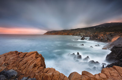 Panoramic view of sea and rocks against sky during sunset