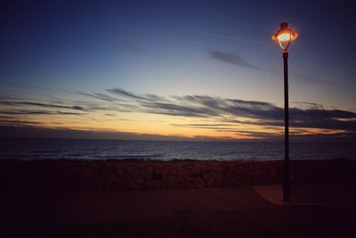 Silhouette street light on beach against sky during sunset