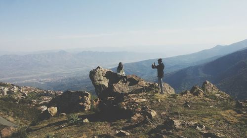 Friends on cliff against mountains during foggy weather