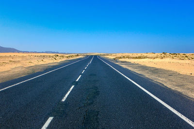 Road passing through desert against clear blue sky