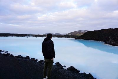 Rear view of man standing by lake against sky