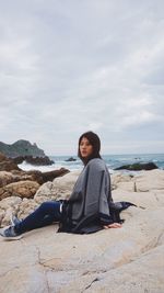 Portrait of woman sitting on rock against cloudy sky