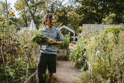 Smiling male farmer with vegetable looking away in community garden