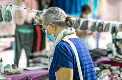 Side view of senior woman wearing mask standing at market stall