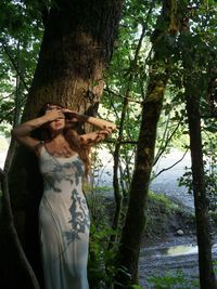 Young woman standing by tree trunk in forest