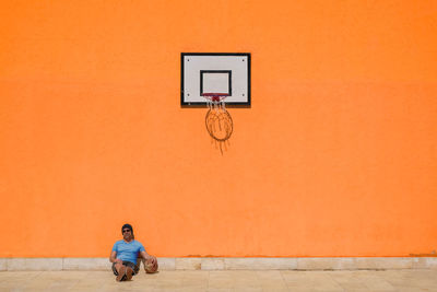 Man sitting on basketball court against orange wall