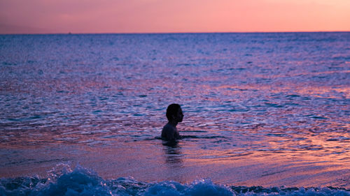 Side view of teenager in sea during sunset