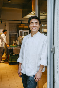 Portrait of happy male chef leaning on door at commercial kitchen