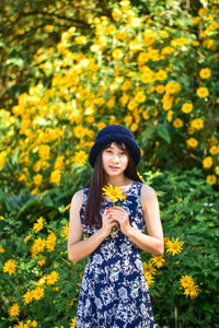 Smiling young woman standing by yellow flowering plants