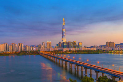 Illuminated buildings by river against sky in city