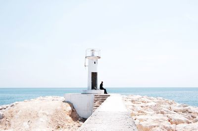 Man sitting by lighthouse at beach