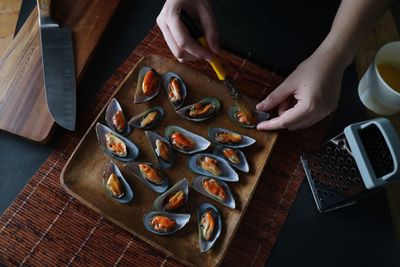 Cropped hands of woman preparing mussels in tray on table