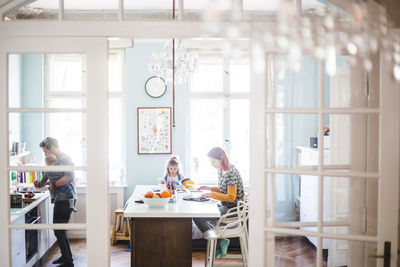 Woman using laptop while sitting with girl studying at kitchen island