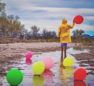 Rear view of boy playing with balloons against sky