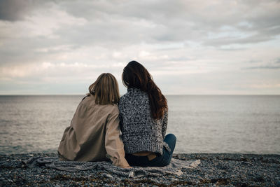 Rear view of female friends spending leisure time at beach against cloudy sky