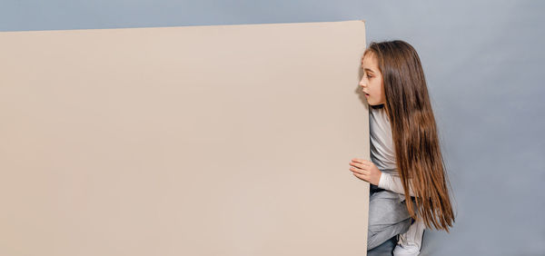 Large sheet of white cardboard. little girl looks surprised at blank banner. advertising.