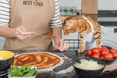 The woman owner and her cat lay out the pizza toppings on the dough.