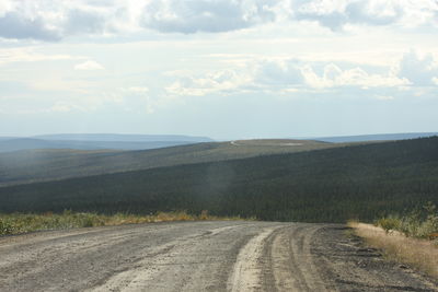 Dirt road amidst landscape against sky