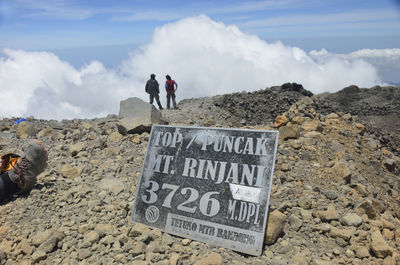 Information sign on mountain peak by hikers against sky