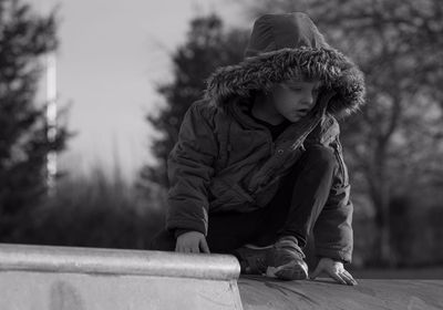 Full length of boy in warm clothing kneeling on footpath against trees