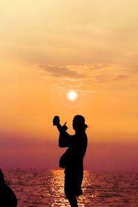 Silhouette man standing by sea against sky during sunset