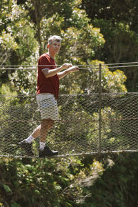 Man walking on rope bridge against trees at forest