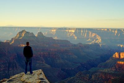 Rear view of man looking at landscape while standing on cliff during sunset