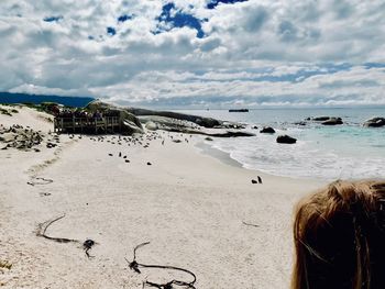 Rear view of woman standing at sandy beach against cloudy sky