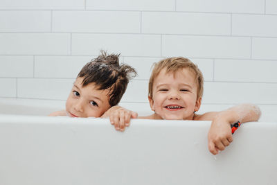 Siblings taking bubble bath in white tub with smiles
