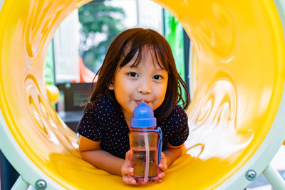 Portrait of cute girl drinking water while lying on outdoor play equipment
